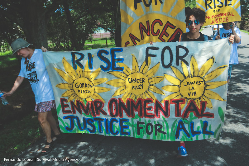 Protestors march with a colorful painted banner that reads "Rise for Environmental Justice for All"