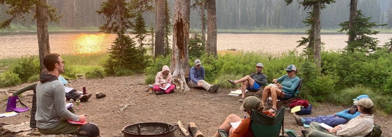 Students sit in a circle next to an alpine lake in Montana