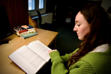 Female student with brown hair and green sweater reading a text book