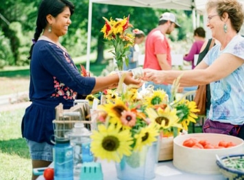 Two women doing a transaction on a outdoor booth.