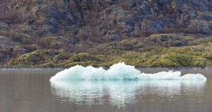 Blue ice floats on a river, with ice-free mountains visible behind.