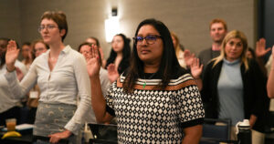 A crowd of students in the Online Hybrid JD program raise their right hands to make the Oath of Professionalism.