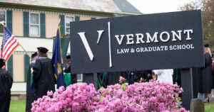 Vermont Law and Graduate School sign with 2025 graduates in the background.