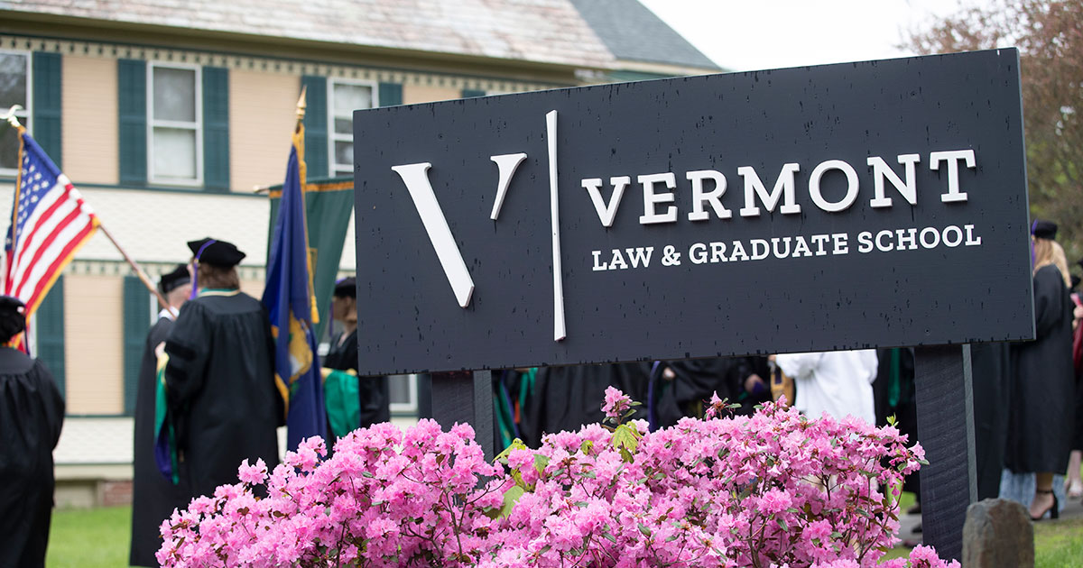 Vermont Law and Graduate School sign with 2025 graduates in the background.